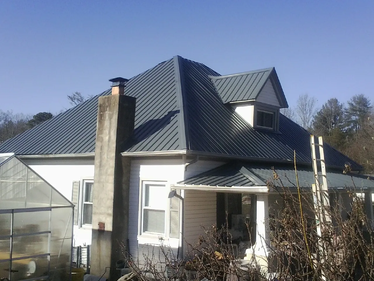 Dark blue standing seam metal roof on a white farmhouse with dormer — Slate & Tile Roof Repair by Roofing Brothers in Tonica