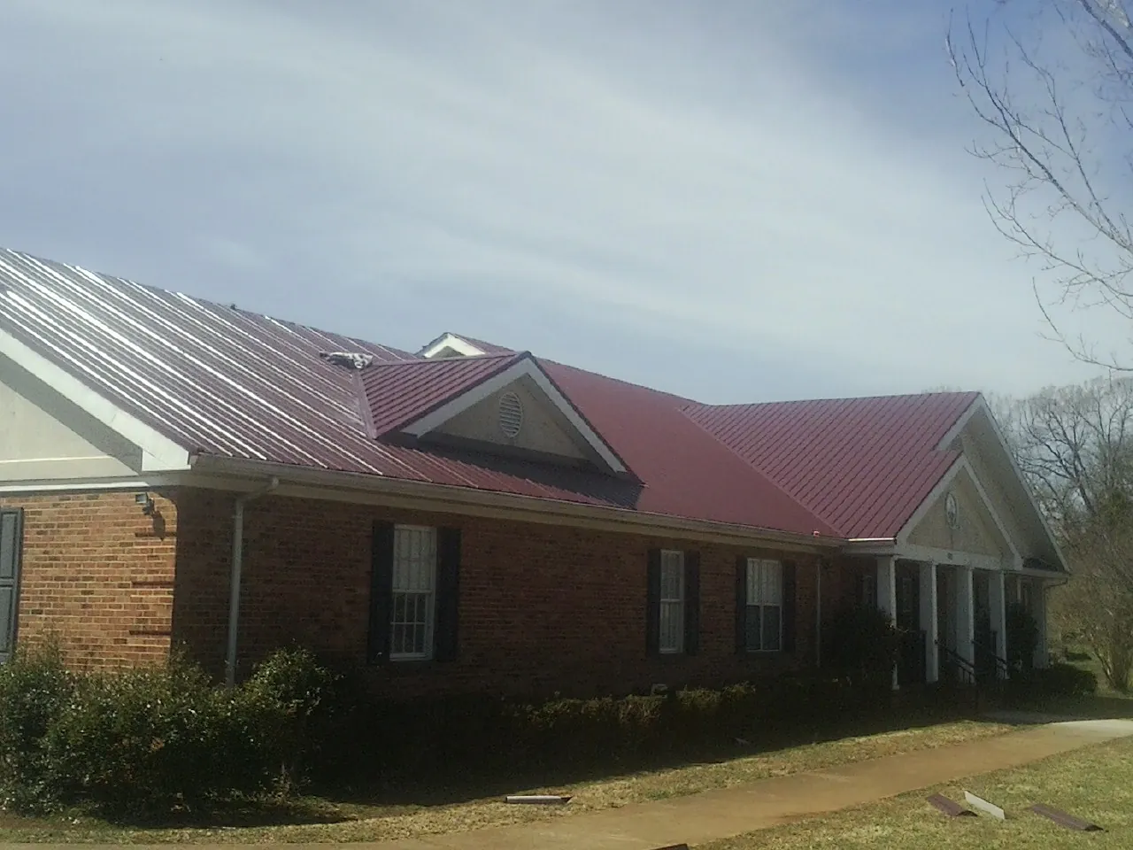 Red metal roof with gabled entries on a long brick building, from a Hail Damage Roof Repair job in Tonica
