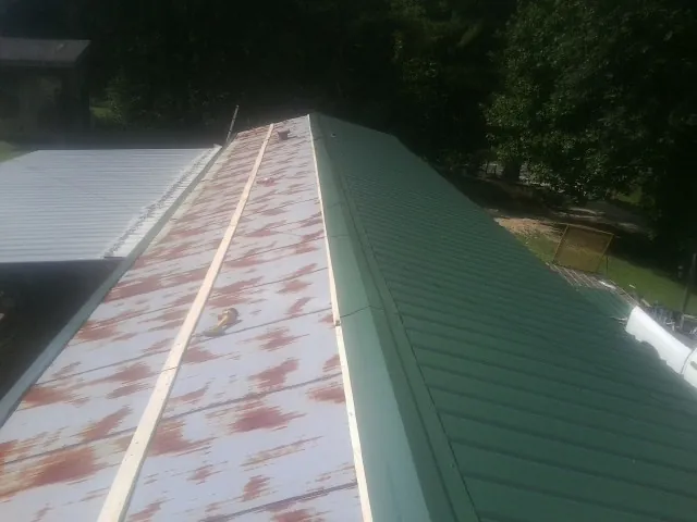 Old rusted panels beside newly installed green metal roofing — Wind Damage Roof Repair by Roofing Brothers in Tonica
