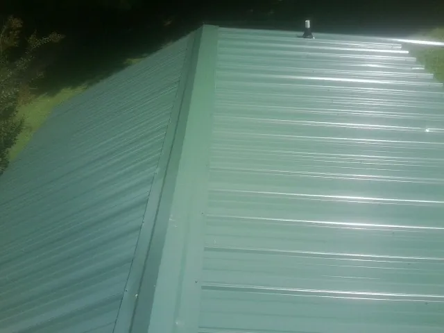 New green metal panels meeting at the ridge of a roof — Flat Roof Repair work by our crew in Tonica