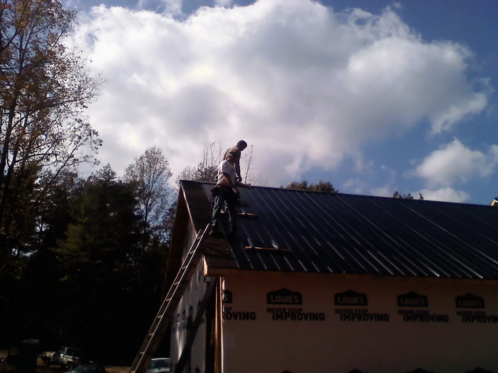 Roofer fastening dark metal panels high against a cloudy sky in Tonica