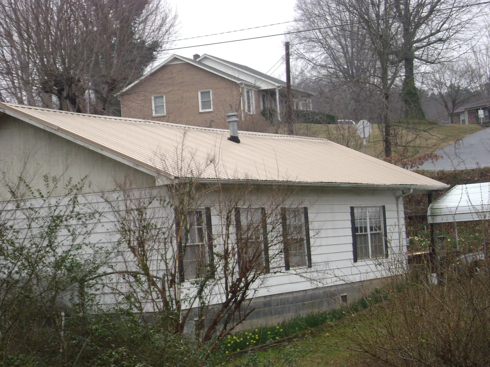 Tan metal roof on a white sided house set into a hillside — Commercial Roofing by Roofing Brothers in Tonica