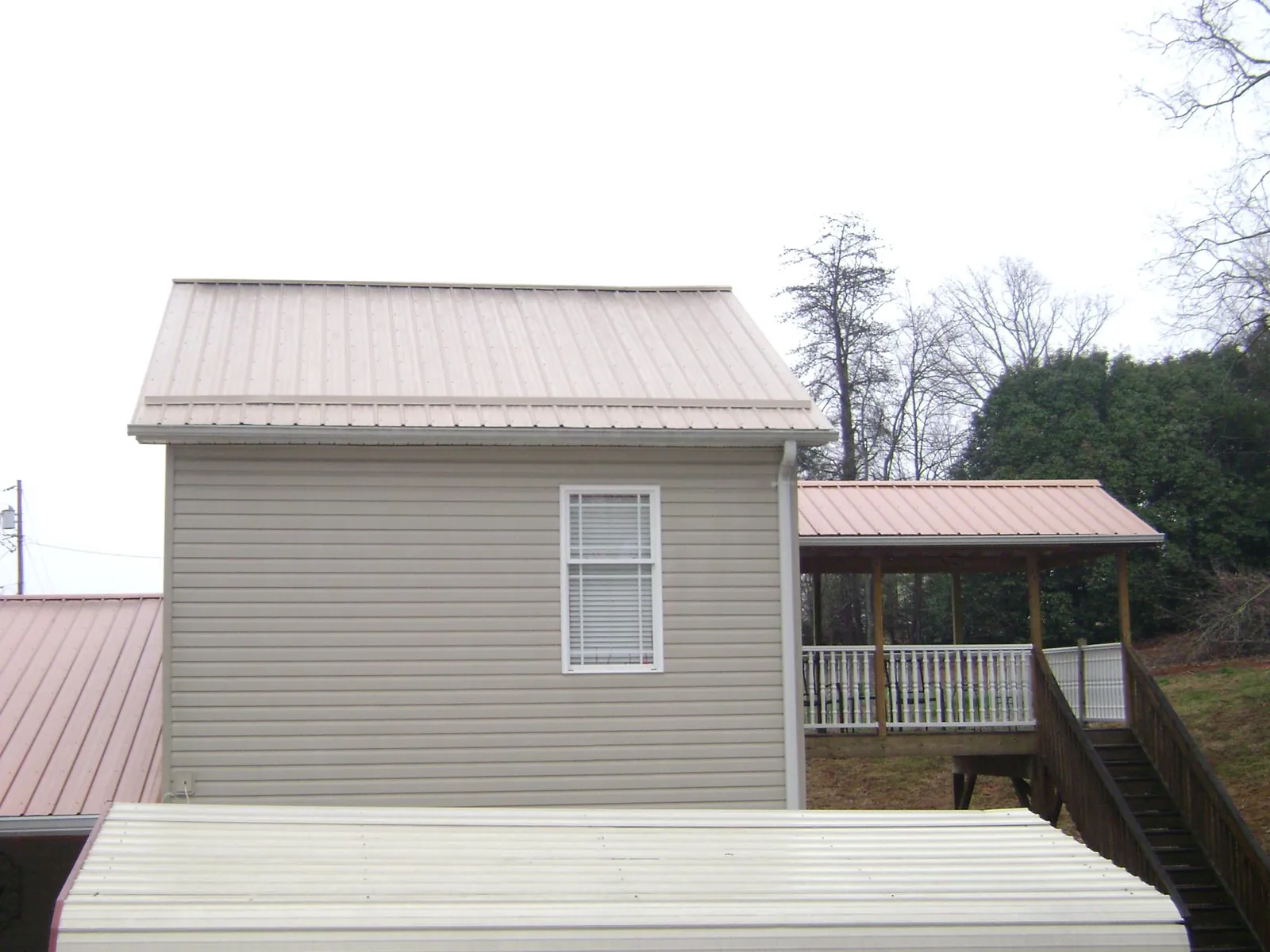 Tan metal roofs on a two story addition and attached porch, from a Roof Replacement job in Tonica